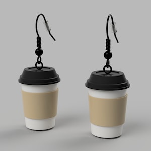 Pode incluir: Um par de brincos de x&iacute;cara de caf&eacute; com tampas pretas e mangas de papel marrom. Os brincos s&atilde;o feitos de metal e t&ecirc;m contas pretas e ganchos.