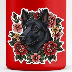 May include: A red tumbler featuring a black dog illustration surrounded by a floral wreath of red, pink, and yellow flowers. The dog has brown eyes and is centered on the tumbler.