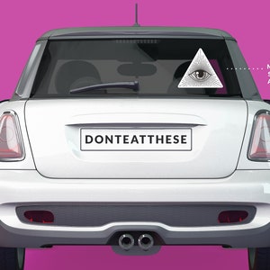 Op de afbeelding: Witte Mini Cooper met een zwart-witte sticker op de achterruit. De sticker is een driehoek met een oog erin. De tekst "DONTEATTHESE" staat op de bumper. Getoond op: Mini Cooper. Getoonde maat: Ongeveer 11 cm