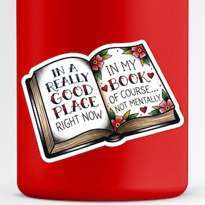 May include: A sticker featuring an open book design with the text "IN A REALLY GOOD PLACE RIGHT NOW" on the left page and "IN MY BOOK OF COURSE... NOT MENTALLY" on the right. The book is decorated with floral and heart accents.