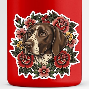 Könnte beinhalten: Ein roter Becher mit einer Illustration eines Deutsch Kurzhaar Hundes, umgeben von roten Rosen, rosa und gelben Blumen. Der Hund hat braune und weiße Markierungen. Das Design ist im Stil traditioneller Tätowierkunst.