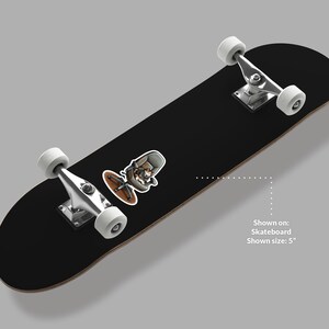 Puede incluir: Monopat&iacute;n negro con ruedas blancas y ejes plateados. Una pegatina con un personaje de dibujos animados en una silla con un disco marr&oacute;n est&aacute; en la tabla. El tama&ntilde;o mostrado es de 12,7 cm.