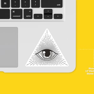 Op de afbeelding: Een zwart-witte sticker van een oog in een driehoek met stralen licht die eruit komen. De sticker is te zien op een 14-inch Macbook Pro-laptop. De sticker is 7,6 cm groot.