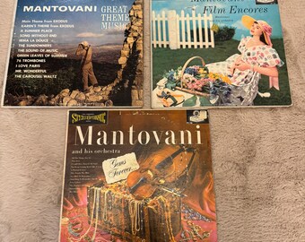 May include: Three vintage vinyl records featuring Mantovani and his orchestra. The first record is titled "Great Theme Music" and features a photo of a rocky landscape. The second record is titled "Film Encores" and features a woman in a white dress sitting in a garden. The third record is titled "Gems Forever" and features a violin and a chest of jewels.