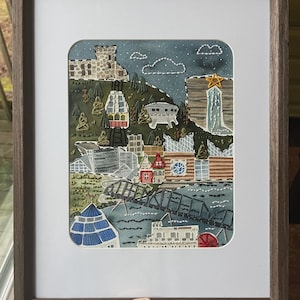 May include: Embroidered artwork depicting a cityscape with a cable car, buildings, a bridge, and a waterfall. The artwork is framed in a dark wood frame.
