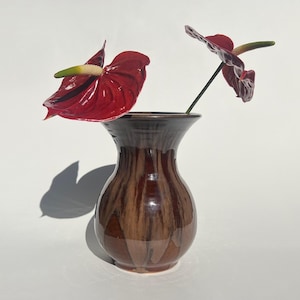 May include: A brown and black striped ceramic vase with two red anthurium flowers.