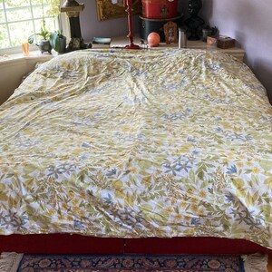 May include: A bed covered with a floral patterned duvet. The duvet features a white background with a repeating pattern of green, yellow, and blue leaves and flowers. The bed frame is red, and a patterned rug is visible at the foot of the bed.