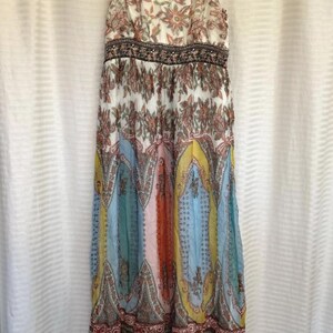 May include: A long, flowing dress with a floral and paisley pattern. The dress features a V-neck, spaghetti straps, and a fitted waist. The skirt has panels of blue, yellow, orange, and pink. The dress is made of a lightweight fabric.