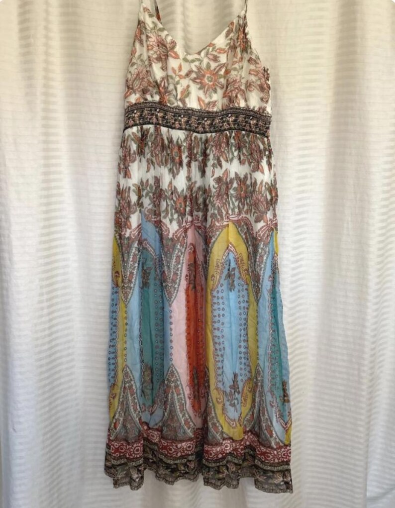 May include: A long, flowing dress with a floral and paisley pattern. The dress features a V-neck, spaghetti straps, and a fitted waist. The skirt has panels of blue, yellow, orange, and pink. The dress is made of a lightweight fabric.