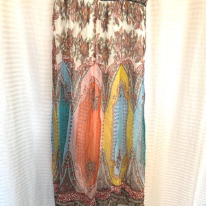 May include: A colorful, patterned dress with a flowing silhouette. The dress features a mix of floral and paisley designs in shades of white, pink, orange, yellow, blue, and teal. The top has a black and brown patterned trim.