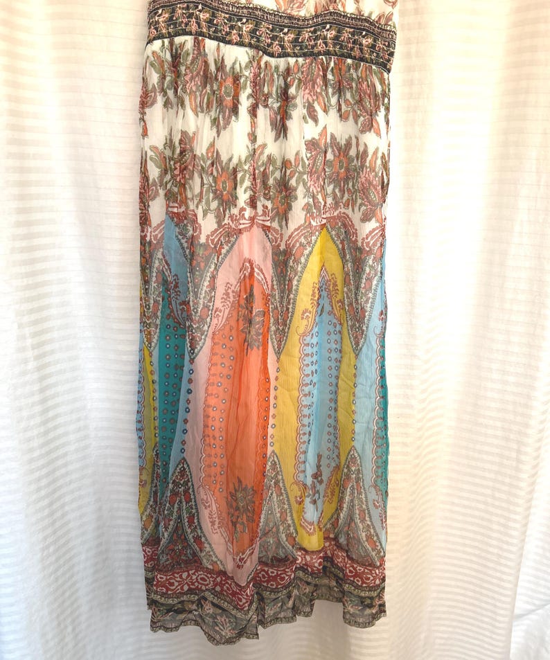 May include: A colorful, patterned dress with a flowing silhouette. The dress features a mix of floral and paisley designs in shades of white, pink, orange, yellow, blue, and teal. The top has a black and brown patterned trim.