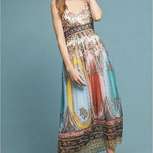 May include: A colorful maxi dress with a floral and paisley print. The dress features a V-neck, spaghetti straps, and a fitted bodice with a patterned waistband. The skirt has vertical panels of yellow, orange, blue, and teal. The dress is worn with gold sandals.
