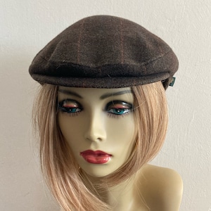 Puede incluir: Una gorra plana de tweed marrón y negro con una visera ligeramente curvada.