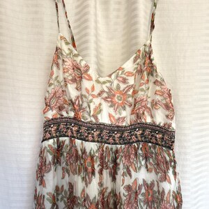 May include: A white sundress with a floral pattern in shades of orange, pink, and green. The dress has thin straps and a fitted bodice with a decorative band. The skirt flows loosely.