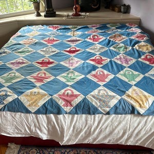 May include: A blue and white quilt with a diamond pattern featuring a variety of colorful baskets. The quilt is made of cotton fabric and is in good condition.