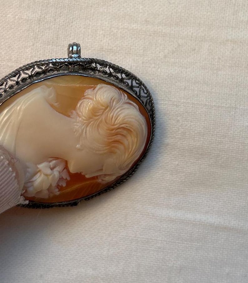May include: A cameo pendant featuring a carved profile of a woman's face, set in a silver filigree frame.