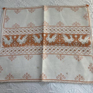 Puede incluir: Camino de mesa de lino blanco con un dise&ntilde;o bordado naranja de p&aacute;jaros estilizados y patrones geom&eacute;tricos.