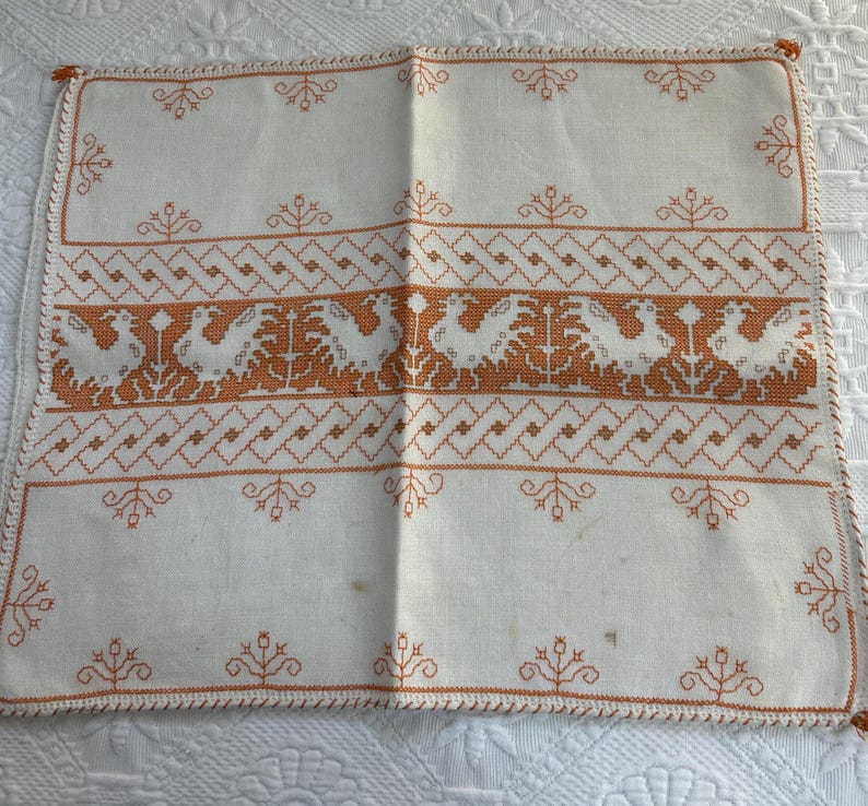 Puede incluir: Camino de mesa de lino blanco con un dise&ntilde;o bordado naranja de p&aacute;jaros estilizados y patrones geom&eacute;tricos.