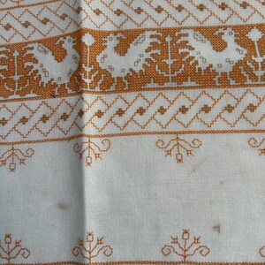 Puede incluir: Mantel de mesa de lino blanco con dise&ntilde;os florales bordados en naranja. El mantel tiene un borde festoneado.