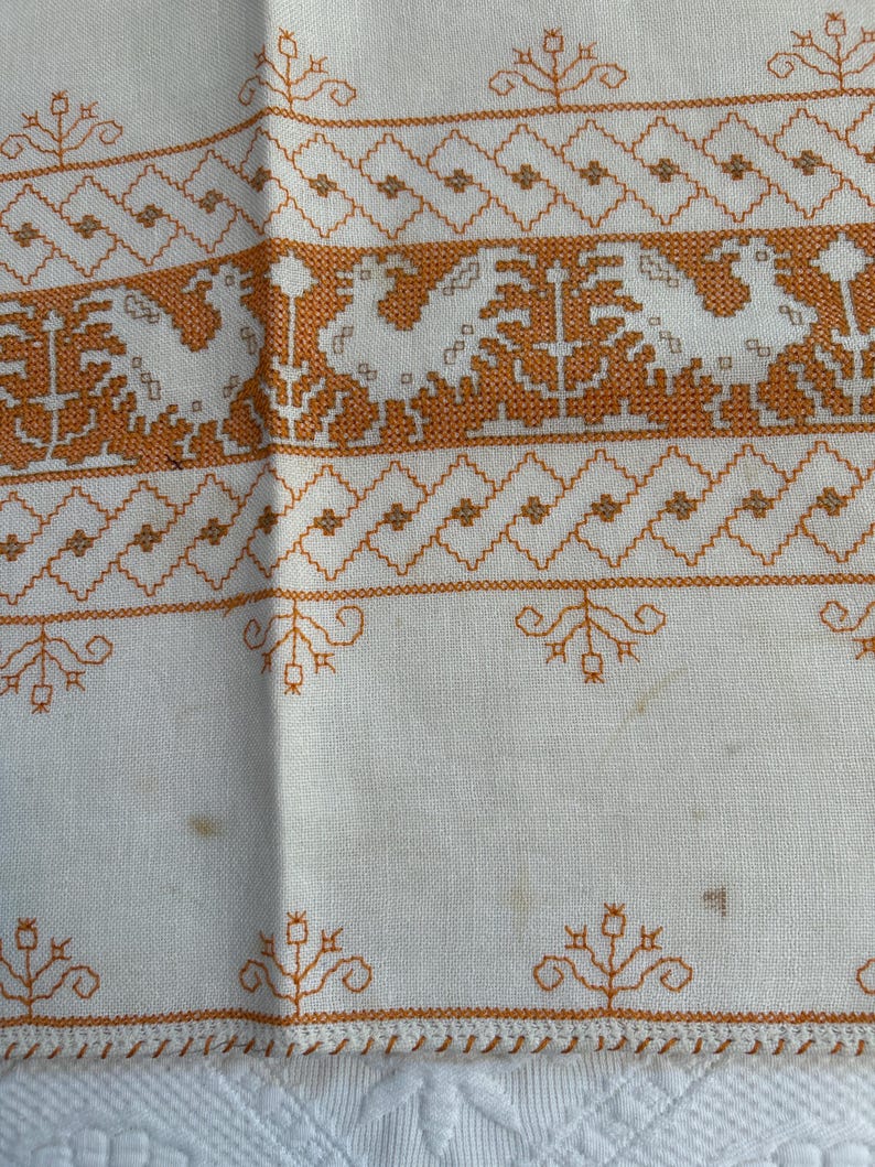 Puede incluir: Mantel de mesa de lino blanco con dise&ntilde;os florales bordados en naranja. El mantel tiene un borde festoneado.