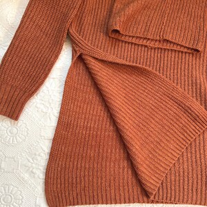May include: Rust-colored knit sweater with a split hem. The long-sleeved sweater has a ribbed texture and a relaxed fit. The garment is made of a soft, warm material, perfect for cooler weather.