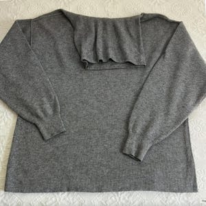 Puede incluir: Su&eacute;ter de punto de canal&eacute; gris con mangas largas y cuello de tortuga.