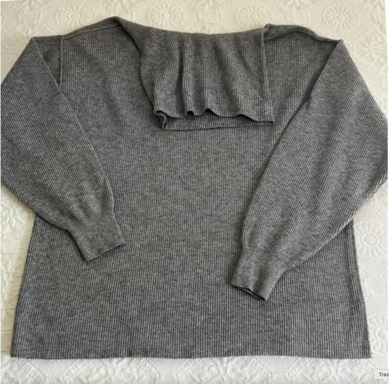 Puede incluir: Su&eacute;ter de punto de canal&eacute; gris con mangas largas y cuello de tortuga.