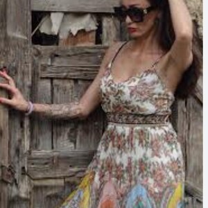 May include: A floral print maxi dress with spaghetti straps. The dress features a white background with a pattern of red and orange flowers. The skirt has a colorful design with blue, orange, and yellow sections. The dress is worn with black sunglasses.