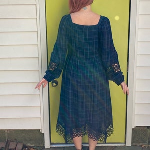 K&ouml;nnte beinhalten: Lang&auml;rmliges Kleid mit Karomuster in Blau-, Gr&uuml;n- und Lilat&ouml;nen. Das Kleid hat einen quadratischen Ausschnitt, Spitzendetails an den &Auml;rmeln und am Saum sowie eine geraffte Taille. Das Kleid ist knielang.