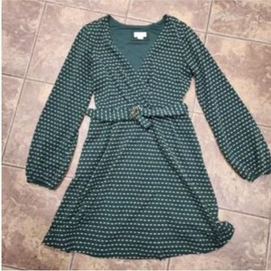 May include: A dark green dress with a white dotted pattern, long sleeves, and a V-neck. The dress features a matching belt with a gold-coloured buckle. The dress is knee-length and made of a lightweight fabric.