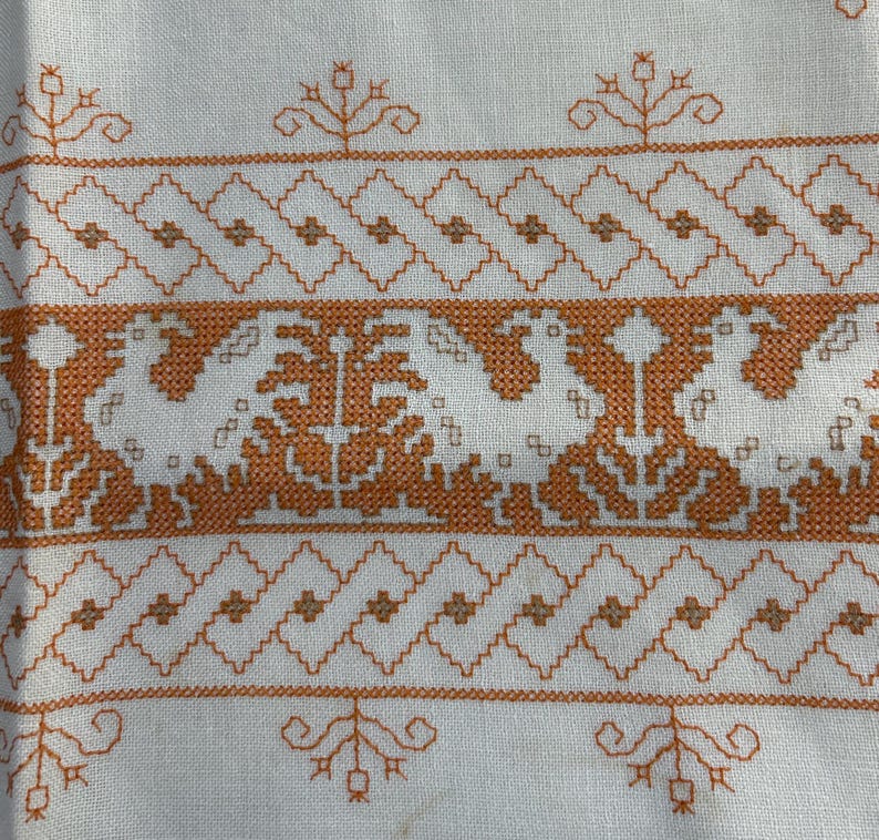 Puede incluir: Tela blanca con un patr&oacute;n repetitivo de costuras bordadas de color naranja. El patr&oacute;n incluye una serie de formas de diamante, peque&ntilde;os motivos florales y dise&ntilde;os m&aacute;s grandes y complejos.