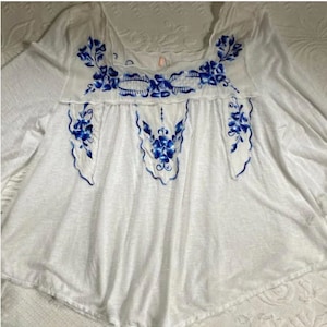 May include: White embroidered blouse with blue floral designs. The blouse has a scoop neck and 3/4 sleeves.