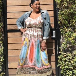 May include: A long, flowing dress with a colorful, abstract design in shades of blue, orange, and yellow. The dress has a floral bodice and is paired with a denim jacket. The dress is worn with gray boots.