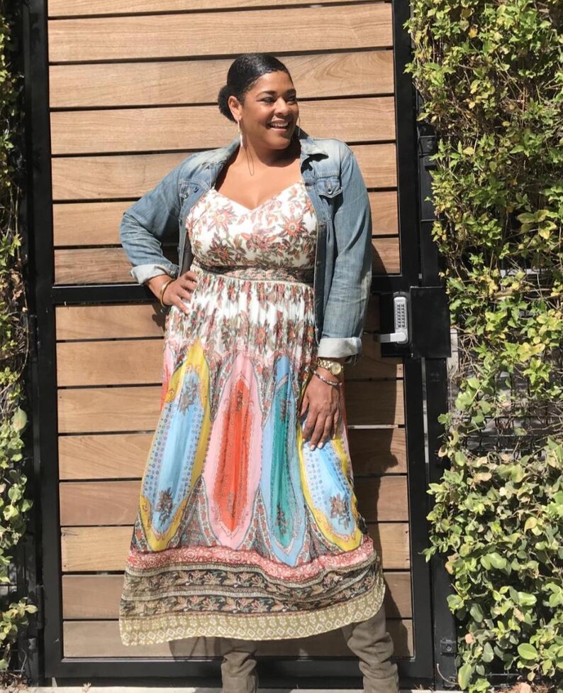 May include: A long, flowing dress with a colorful, abstract design in shades of blue, orange, and yellow. The dress has a floral bodice and is paired with a denim jacket. The dress is worn with gray boots.