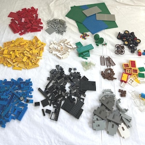 May include: An assortment of colorful plastic building blocks, including red, yellow, blue, gray, and black pieces. The image also shows green baseplates, wheels, and small figures, ideal for creative construction and play.