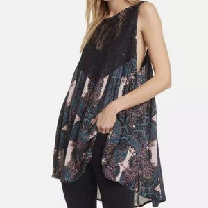 May include: A sleeveless, black and blue paisley print tunic with a black lace overlay at the neckline. The tunic has a high neckline and a loose, flowing fit.