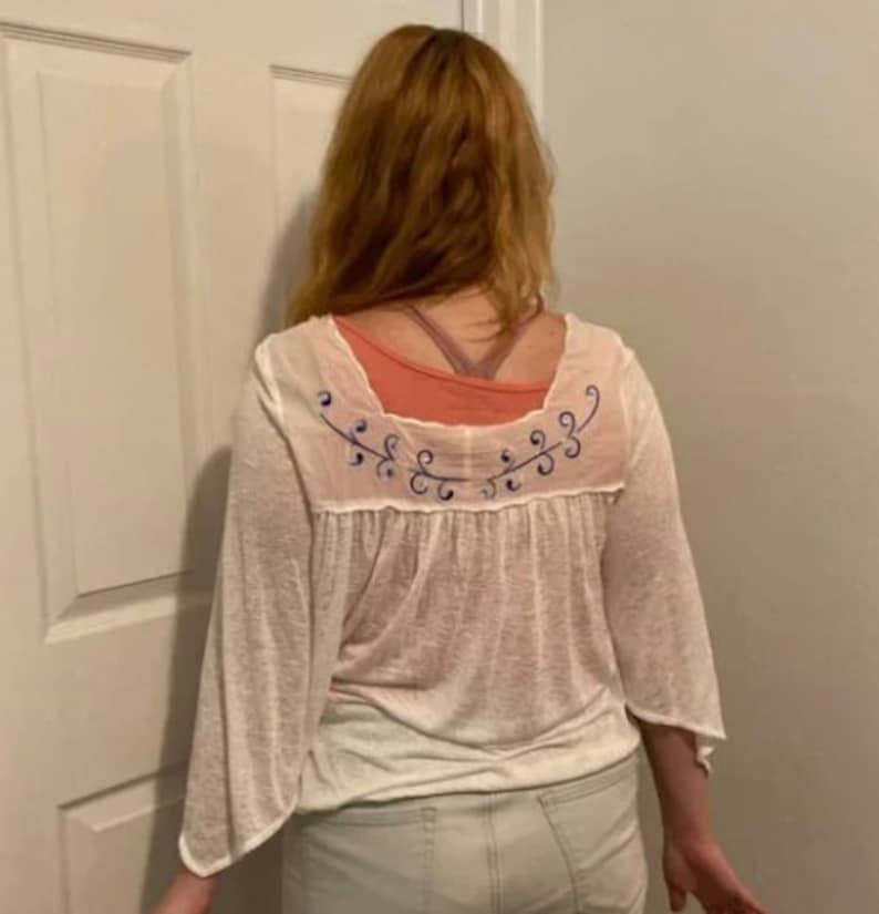 May include: White sheer blouse with a blue floral embroidery design on the back. The blouse has a scoop neck and 3/4 sleeves.
