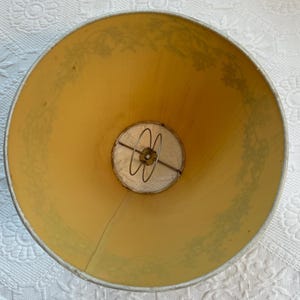K&ouml;nnte beinhalten: Ein Vintage-Lampenschirm mit hellgelbem Innenraum und einem floralen Muster in ged&auml;mpftem Gr&uuml;n. Der Lampenschirm hat einen Metallrahmen und einen wei&szlig;en Stoffdiffusor am Boden. Die Gesamtform ist ein klassischer Kegel.