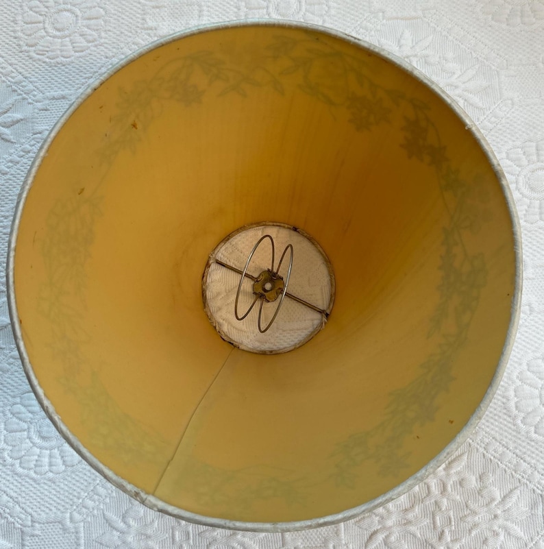 K&ouml;nnte beinhalten: Ein Vintage-Lampenschirm mit hellgelbem Innenraum und einem floralen Muster in ged&auml;mpftem Gr&uuml;n. Der Lampenschirm hat einen Metallrahmen und einen wei&szlig;en Stoffdiffusor am Boden. Die Gesamtform ist ein klassischer Kegel.