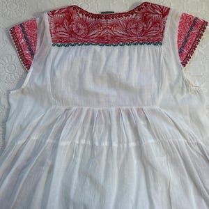 Op de afbeelding: Wit katoenen boerenblouse met rode en groene borduursels rond de halslijn en op de korte mouwen.
