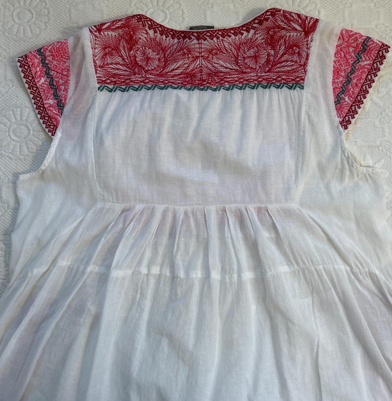 Op de afbeelding: Wit katoenen boerenblouse met rode en groene borduursels rond de halslijn en op de korte mouwen.