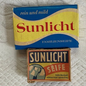 May include: Two vintage Sunlight soap boxes. The larger box is blue and yellow with the word "Sunlicht" in red. The smaller box is brown and yellow with the words "Sunlicht Seife". Both boxes have text in German.