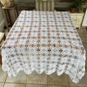 Könnte beinhalten: Weiße Häkeltischdecke mit einem zarten Blumenmuster. Die Tischdecke liegt auf einem Holztisch.