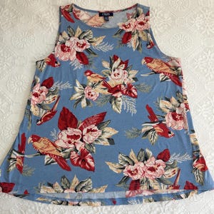 May include: A sleeveless blue tank top with a floral and bird print. The top features a pattern of red, pink, and white flowers, along with tan and red birds. The brand name "CHAPS" is visible near the neckline.