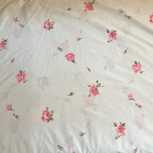 Puede incluir: Tela blanca con un estampado de rosas rosas y hojas verdes. Las rosas varían en tamaño y están dispersas por la superficie. Algunas rosas están en plena floración, mientras que otras son capullos. La tela parece ligeramente arrugada.