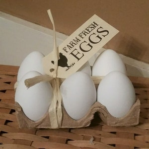 May include: A carton of six white farm fresh eggs tied with twine and a brown paper tag that reads "Farm Fresh Eggs".