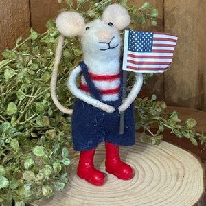 May include: A white felt mouse wearing red boots and a red and white striped shirt holds a small American flag.