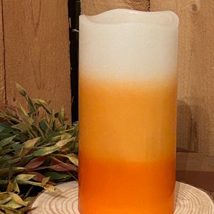 May include: A white, orange, and yellow ombre pillar candle. The candle is on a wooden slice.