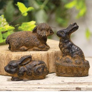 May include: Three rustic, brown-toned animal figurines: a lamb and two rabbits. The lamb is lying down, while one rabbit sits upright and the other is in a resting pose. The figurines have a textured, aged appearance, suggesting they are made of cast iron or a similar material.