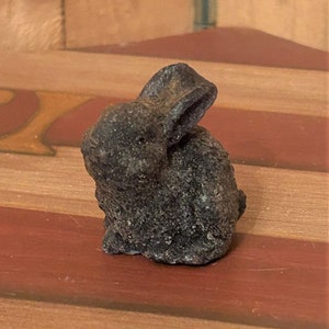May include: A small, black, ceramic rabbit figurine with a textured surface.